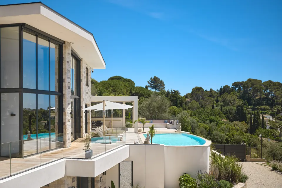 Contemporary hillside villa: glazed openings over two floors, stone cladding, a glass-edged terrace and a curved infinity pool above the greenery.