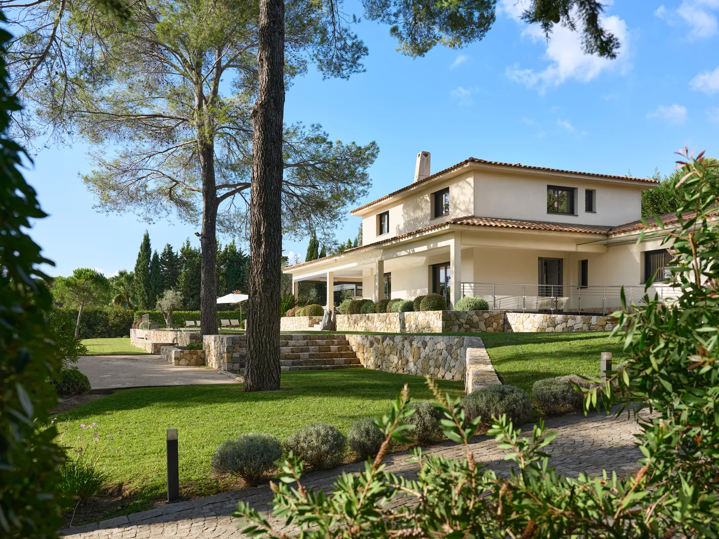 Villa à étage aux façades claires vue entre les pins, escalier en pierre et pelouse