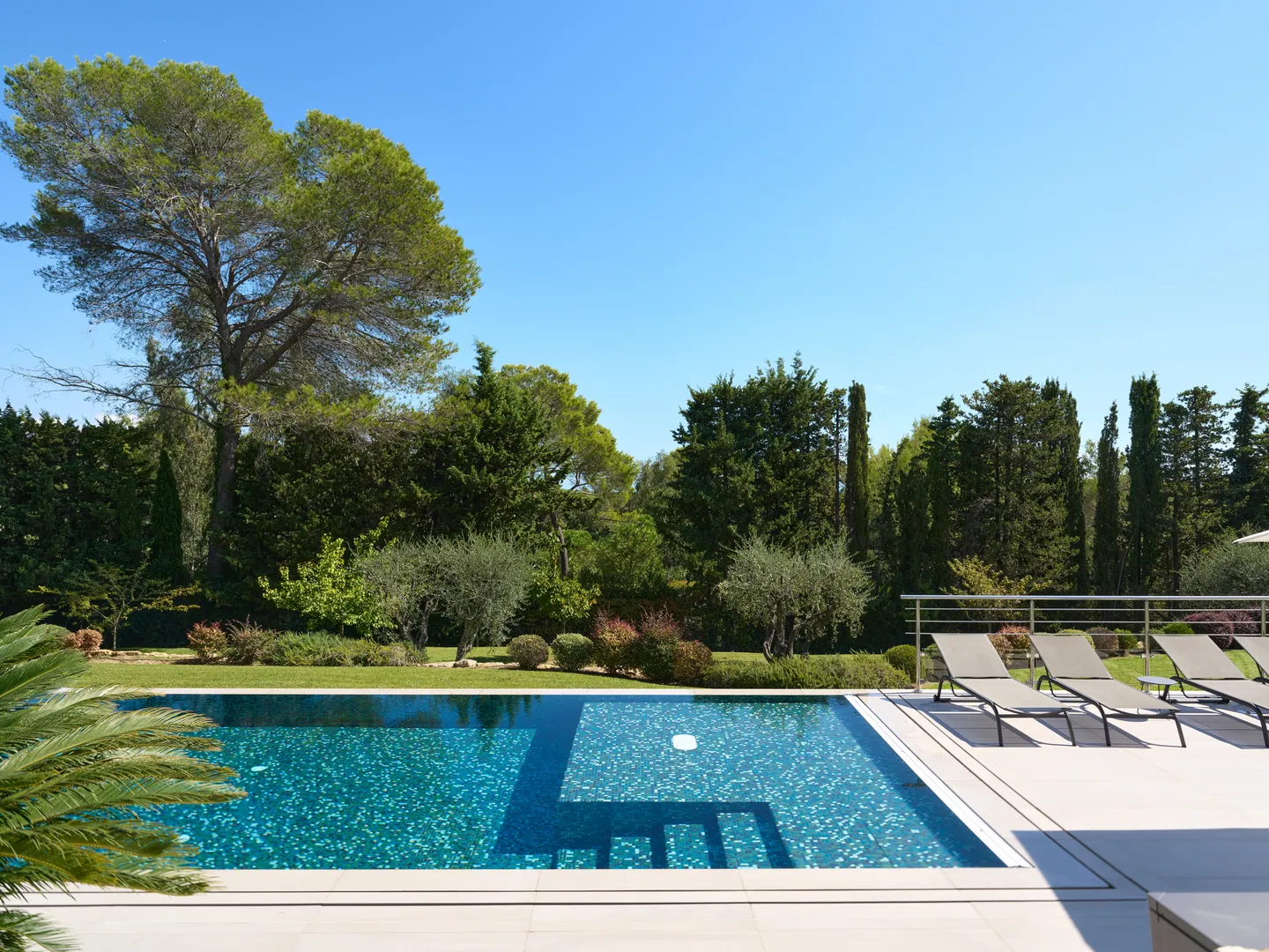 Piscine en mosaïque bleue et bains de soleil face au jardin arboré