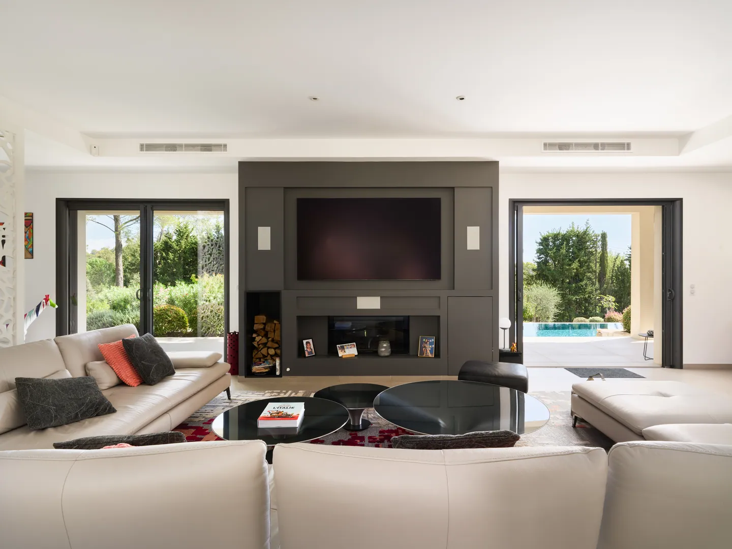 Salon avec meuble TV et cheminée encastrés, baies ouvertes sur la piscine