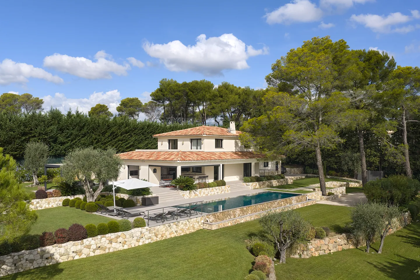 Villa aux tuiles rouges vue en hauteur, piscine à débordement et jardin en restanques bordé de pins