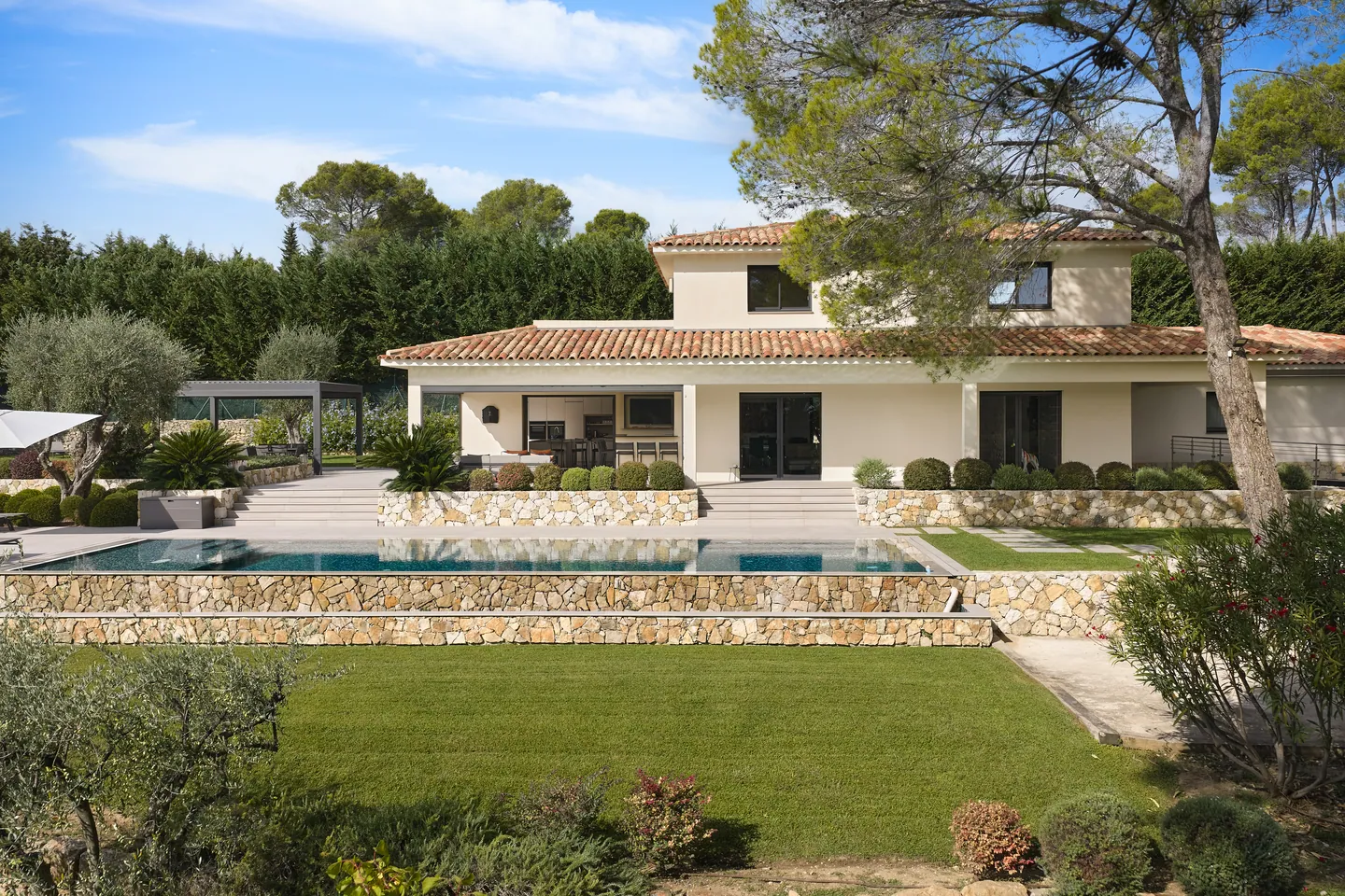 Façade côté jardin avec piscine sur muret en pierre sèche et pelouse au premier plan