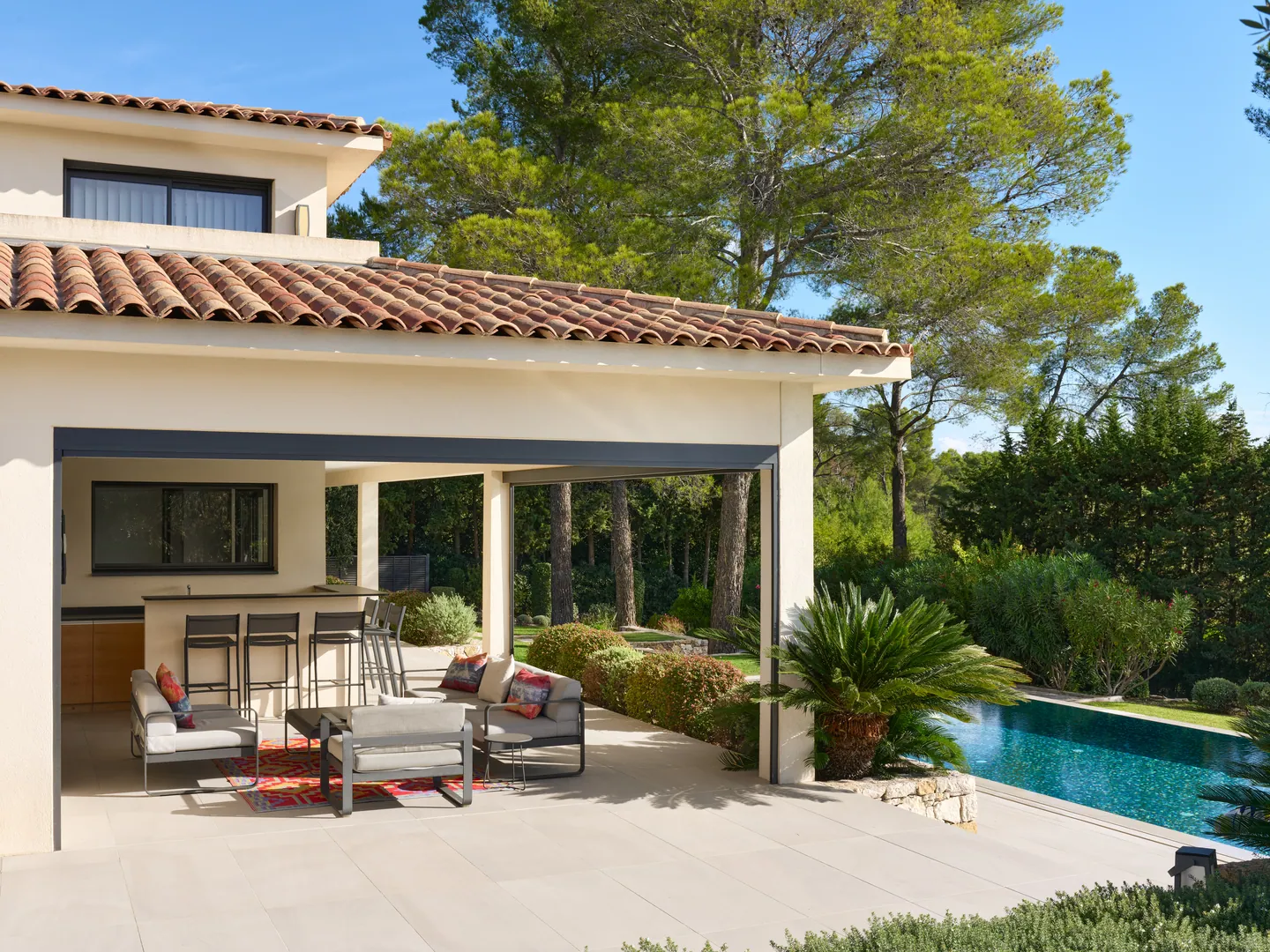 Terrasse couverte avec salon d'extérieur et bar, piscine en contrebas