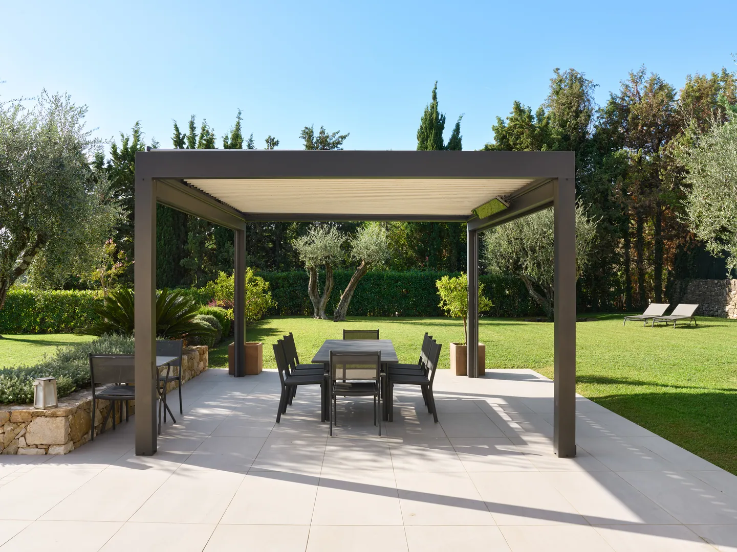 Pergola bioclimatique abritant une table à manger sur terrasse dallée