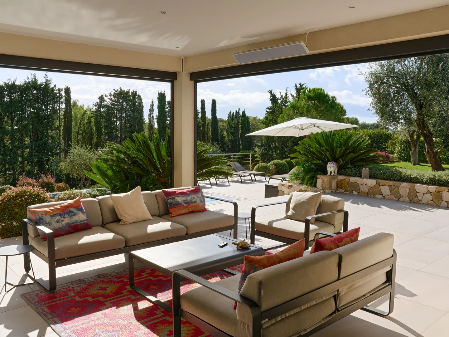 Salon d'extérieur ouvert sur le jardin, la piscine et le parasol