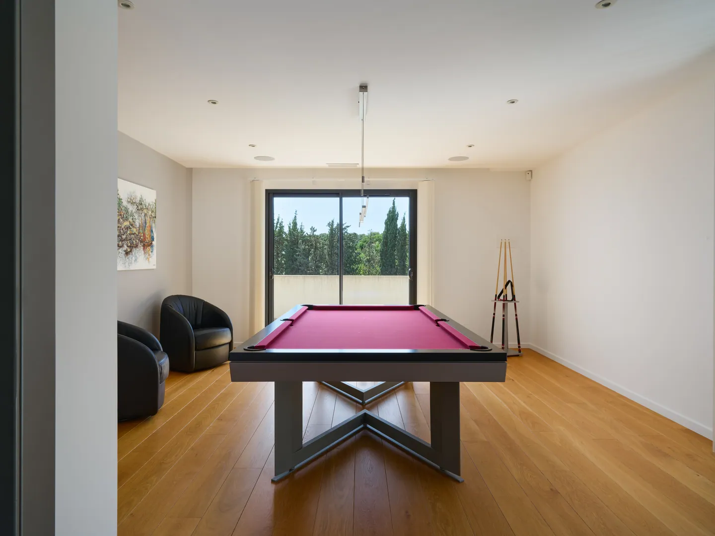 Salle de billard au parquet chêne, fauteuils en cuir et baie vitrée