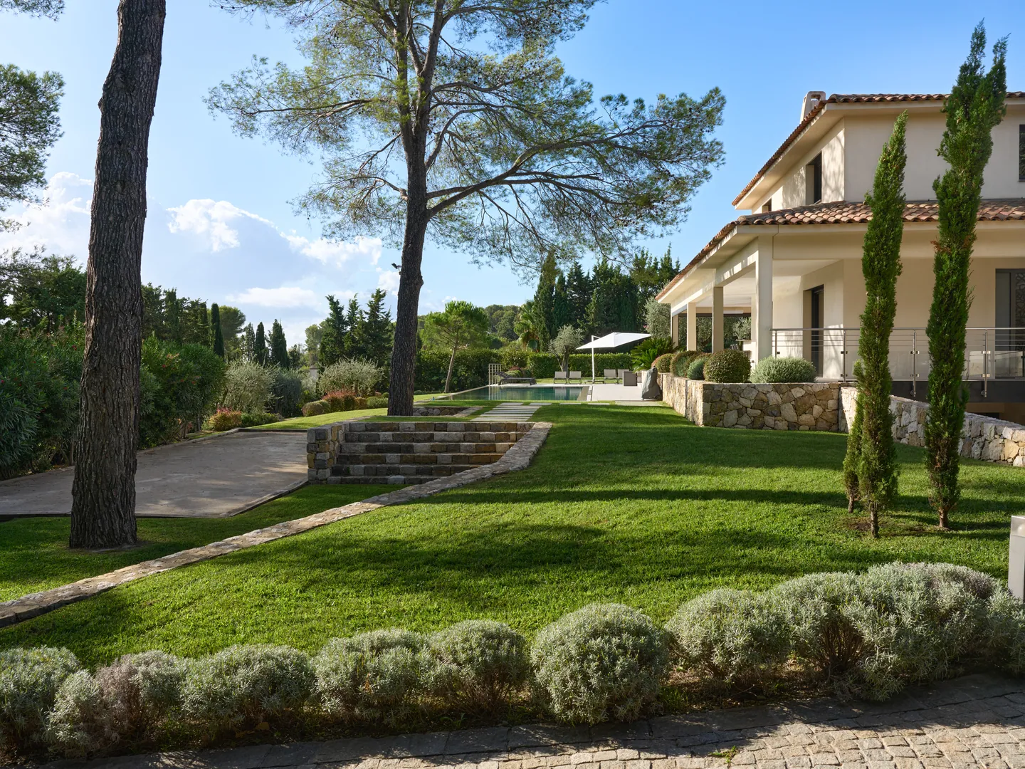 Jardin en pente avec pins, cyprès et lavandes, terrasse de la villa à droite