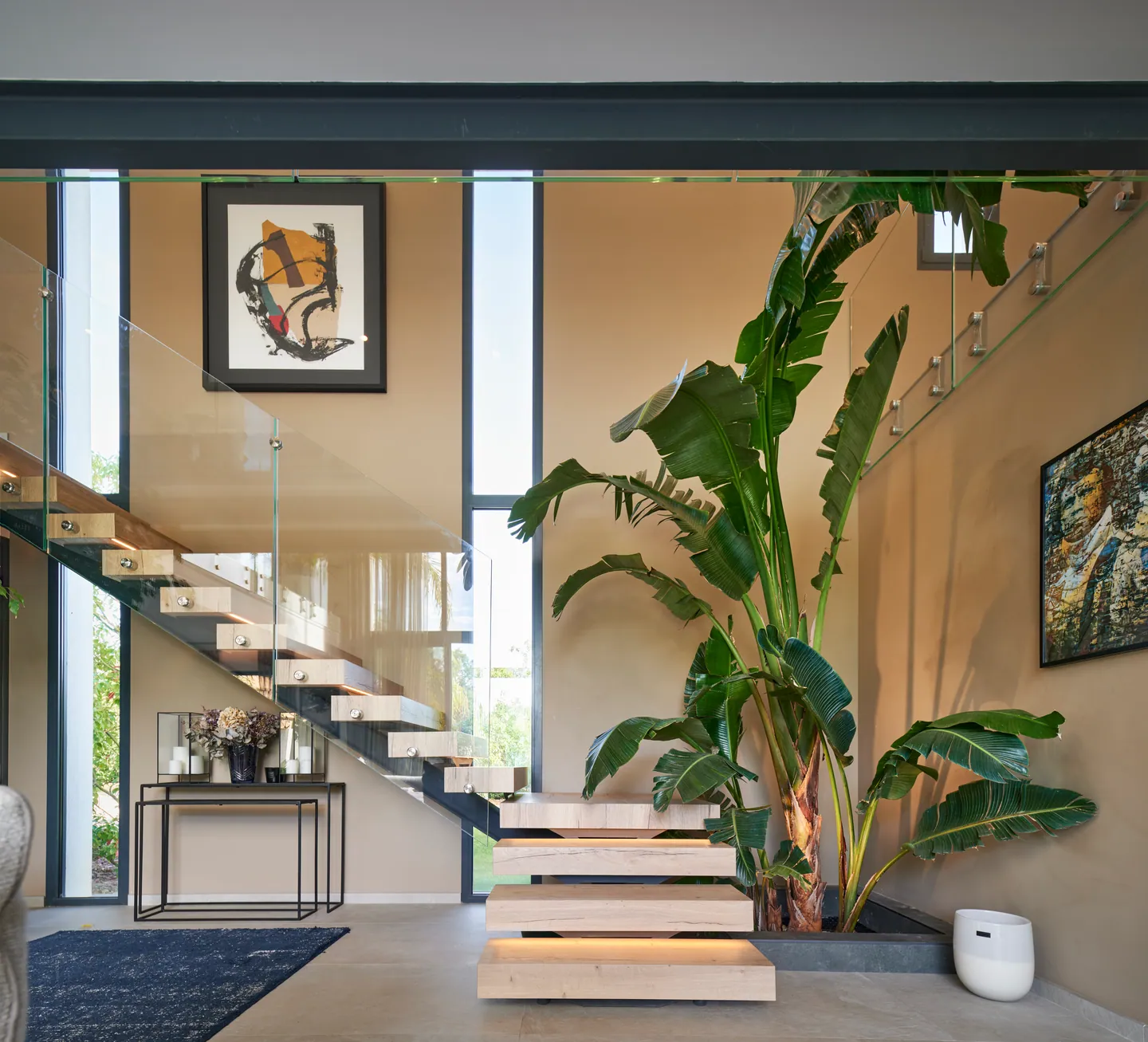 Escalier suspendu en chêne et garde-corps en verre, bananier d'intérieur et fenêtres verticales