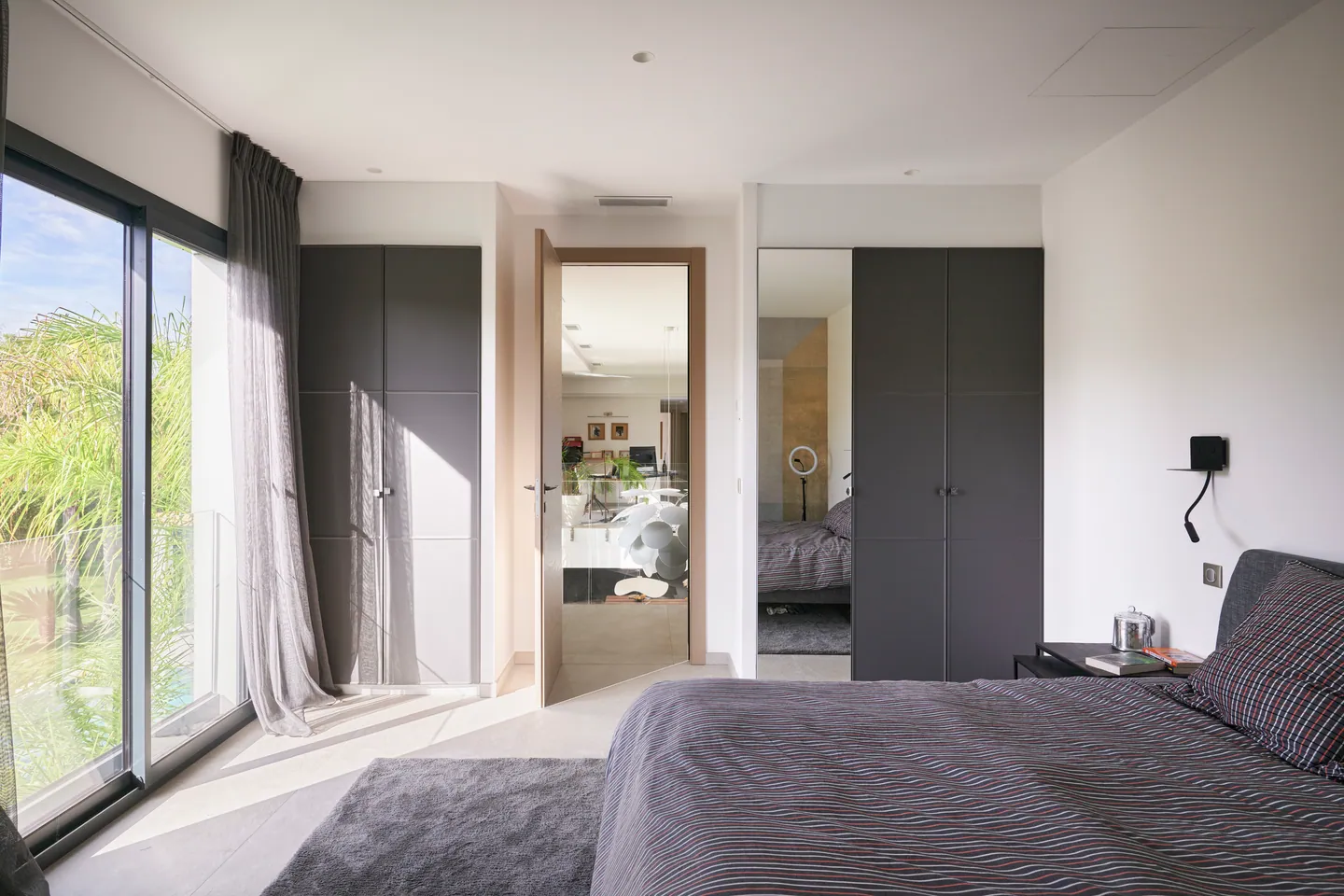 Chambre avec baie vitrée sur les palmiers, placards anthracite et porte ouverte sur l'étage