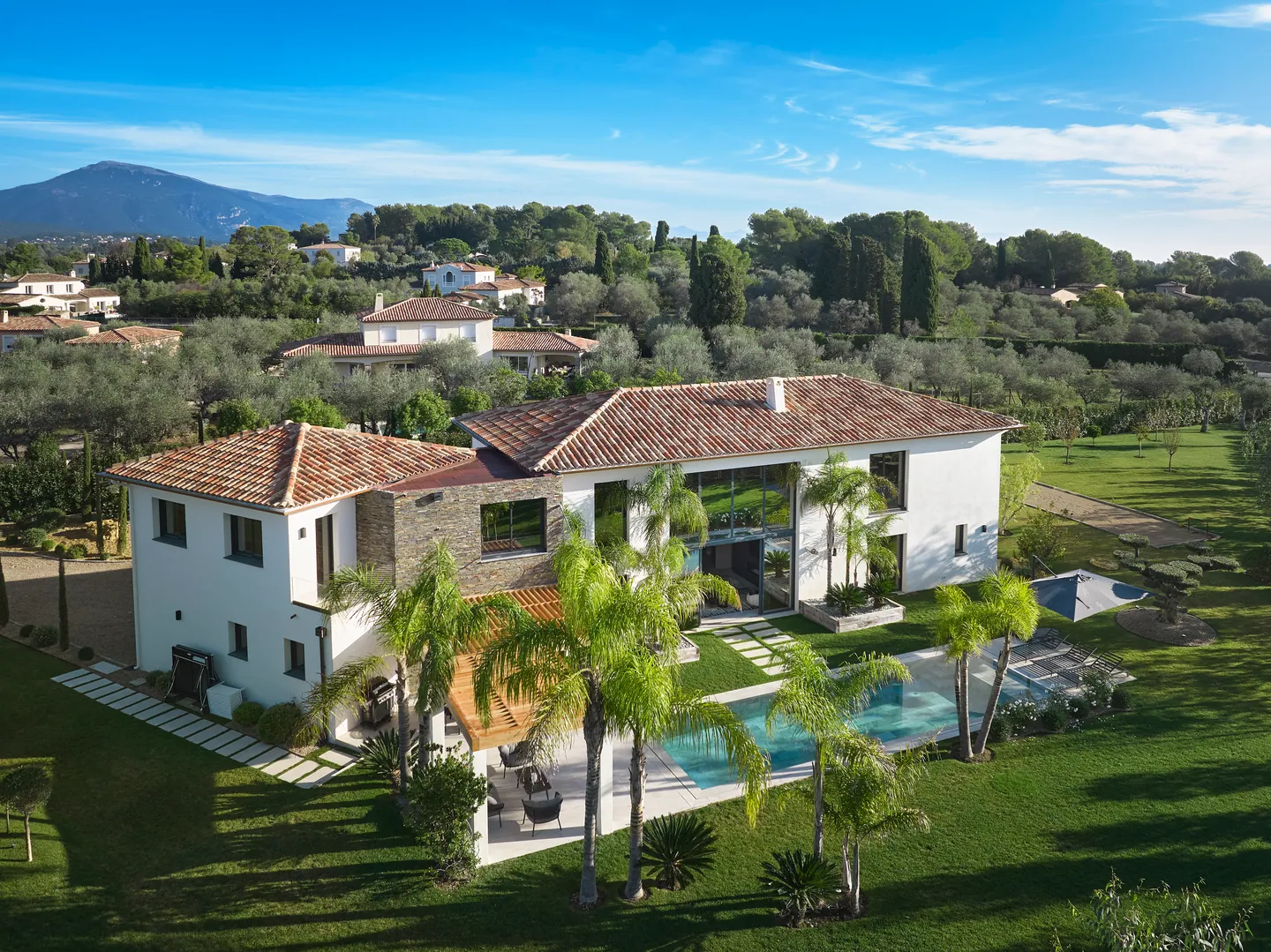 Vue aérienne de la villa blanche aux toits de tuiles, piscine bordée de palmiers et jardin d'oliviers