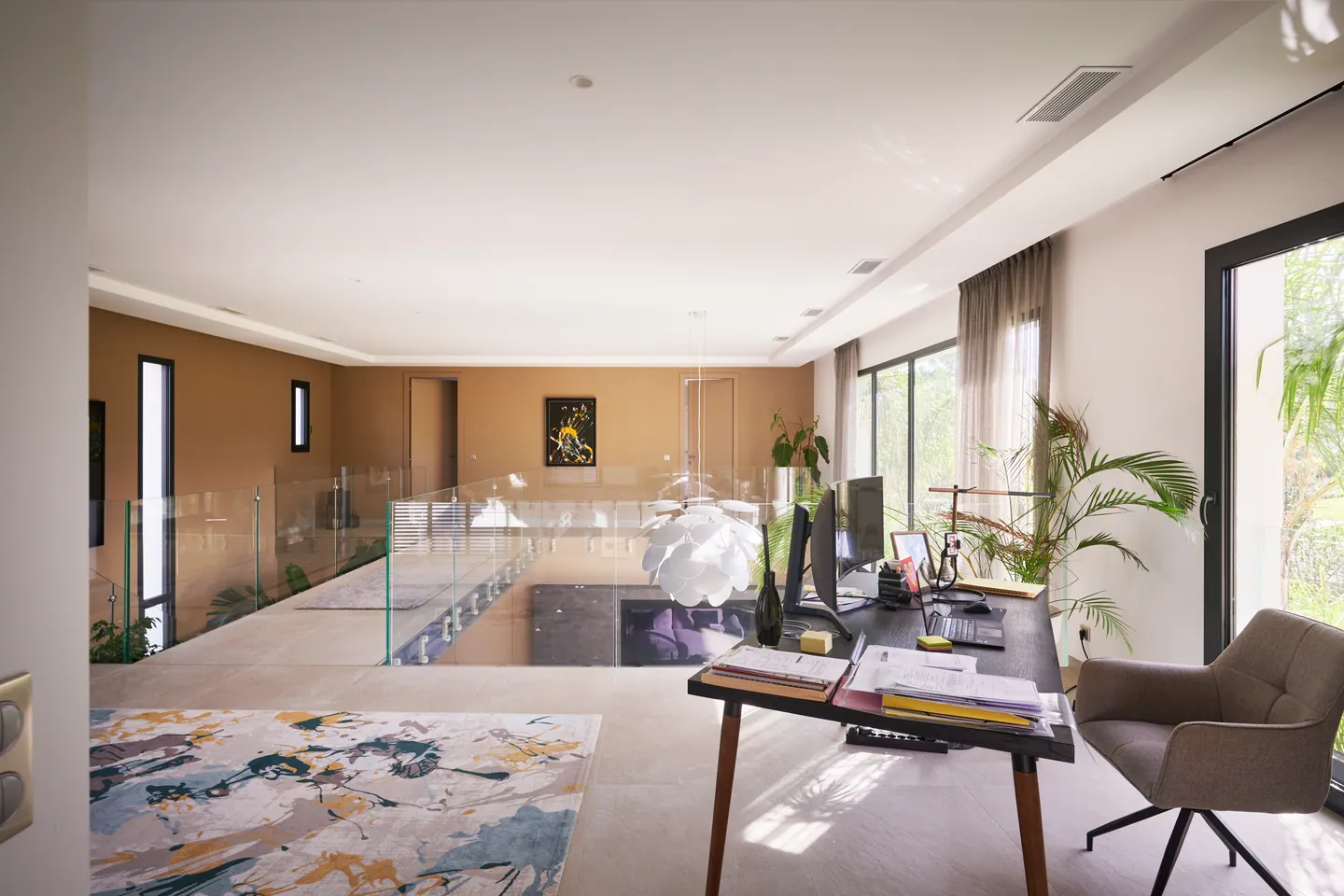 Bureau aménagé en mezzanine avec garde-corps en verre et grandes baies sur le jardin