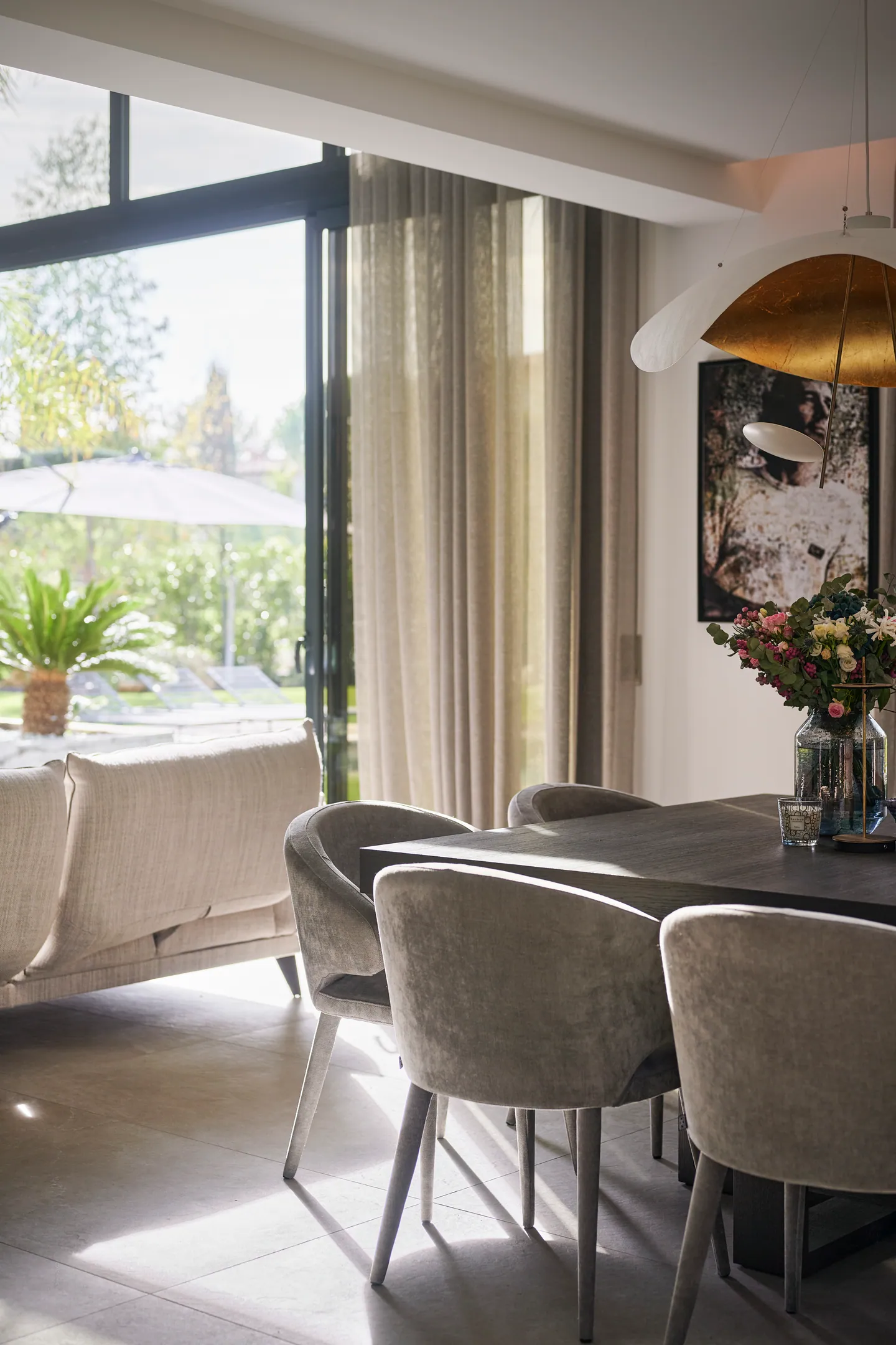 Coin repas baigné de lumière, suspension dorée, bouquet de fleurs et baie ouverte sur la terrasse
