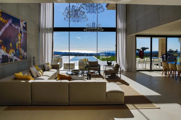 Salon double hauteur ouvert par une grande baie vitrée sur la piscine et la vue mer