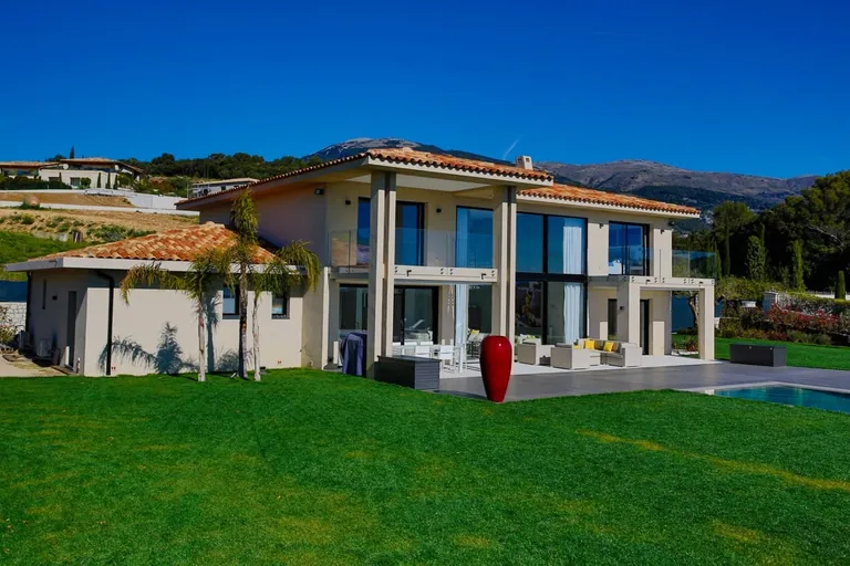 Vue de trois quarts de la villa depuis la pelouse, avec la terrasse et la piscine