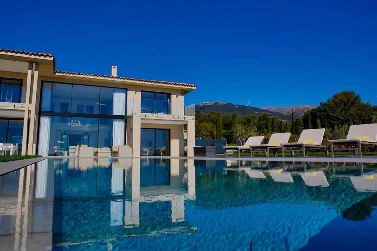 La piscine au premier plan, où se reflètent la façade et les bains de soleil