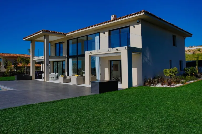 La villa de trois quarts depuis le jardin, avec terrasse couverte et balcon vitré
