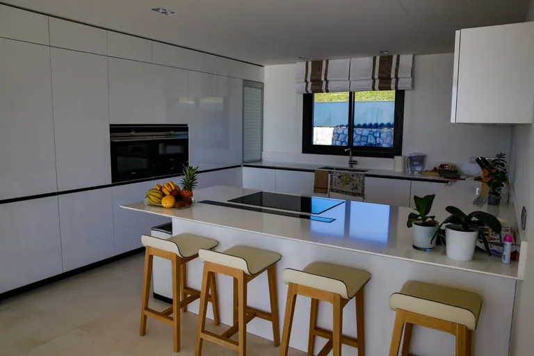 Cuisine blanche avec îlot central, plaque de cuisson et tabourets en bois