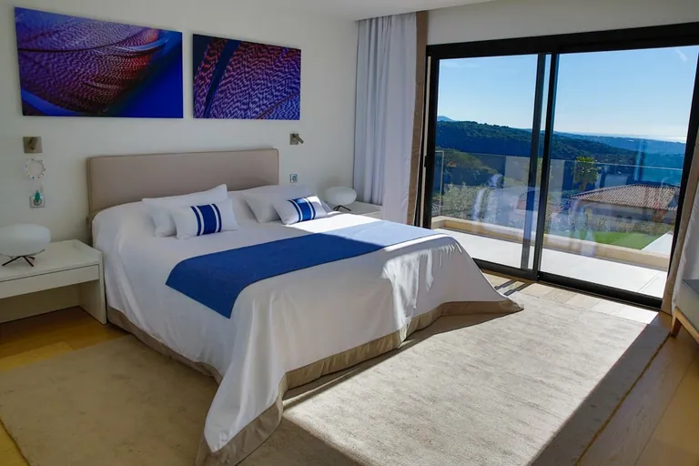 Chambre avec lit double et baie vitrée sur un balcon face aux collines