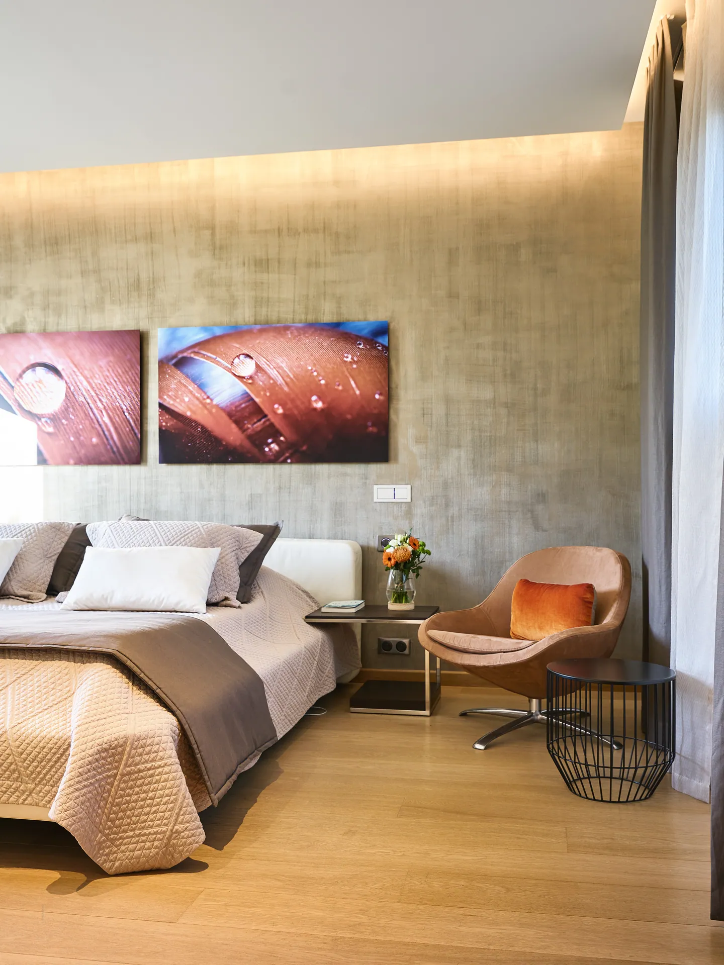 Bedroom with textured wall, artworks, armchair and oak floor