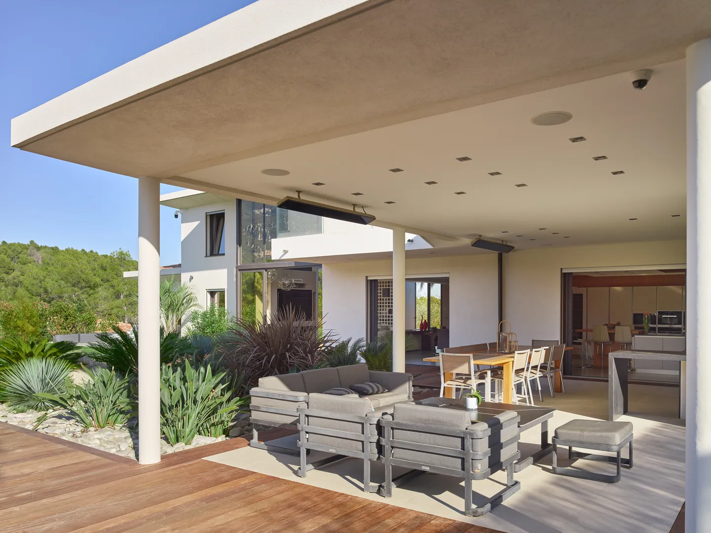 Covered terrace with outdoor lounge and dining table, open kitchen beyond