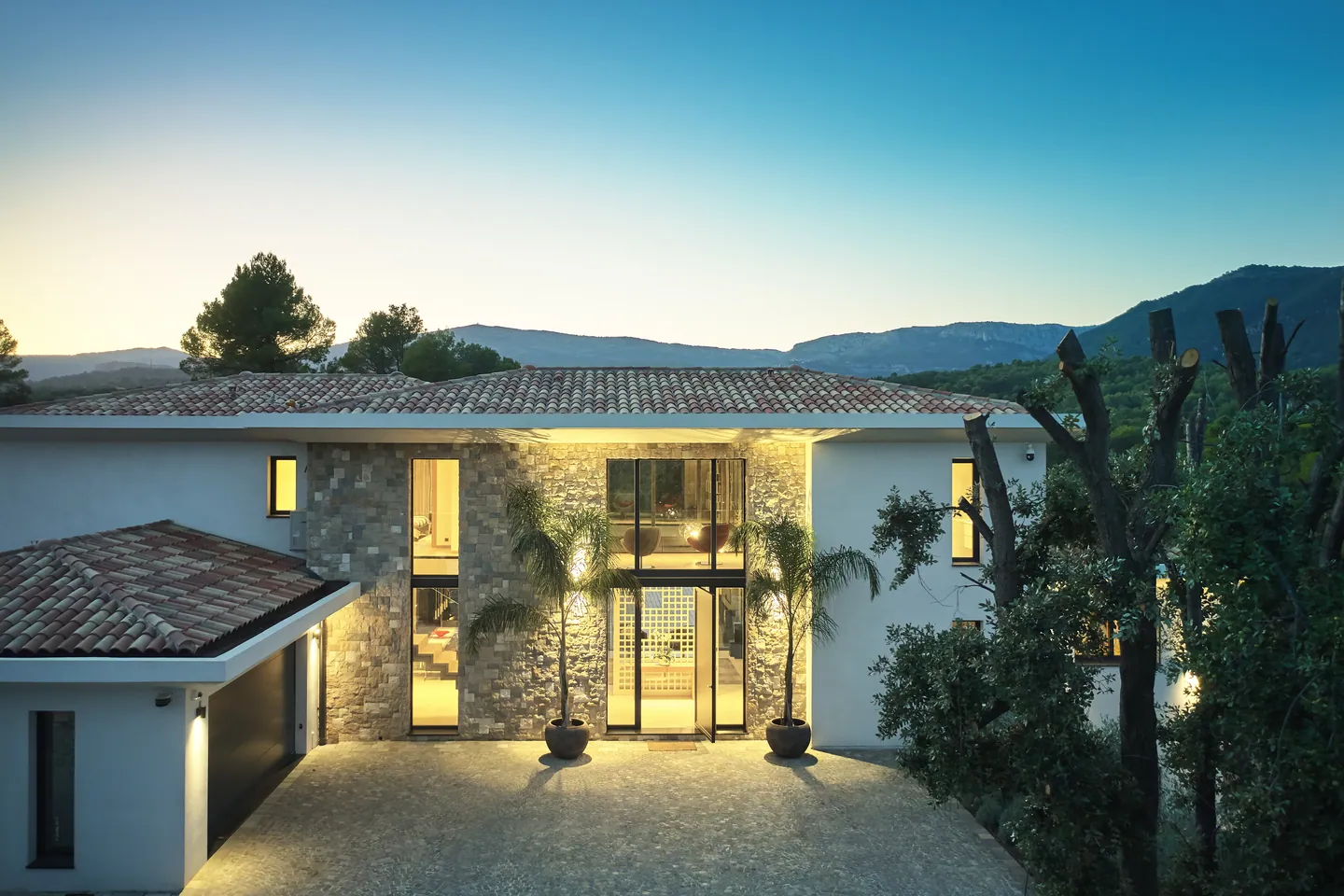 Entrance facade lit at dusk, stone cladding and mountains