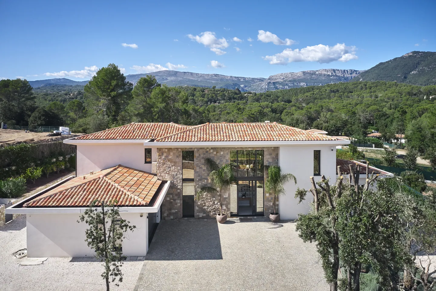 Elevated view of tiled villa with stone cladding, entrance courtyard and mountains behind