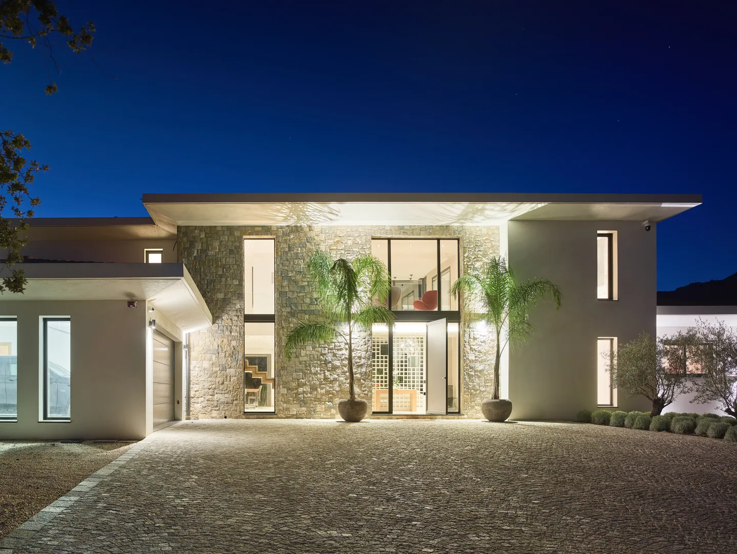Entrance facade lit at blue hour, cobbled courtyard and palms