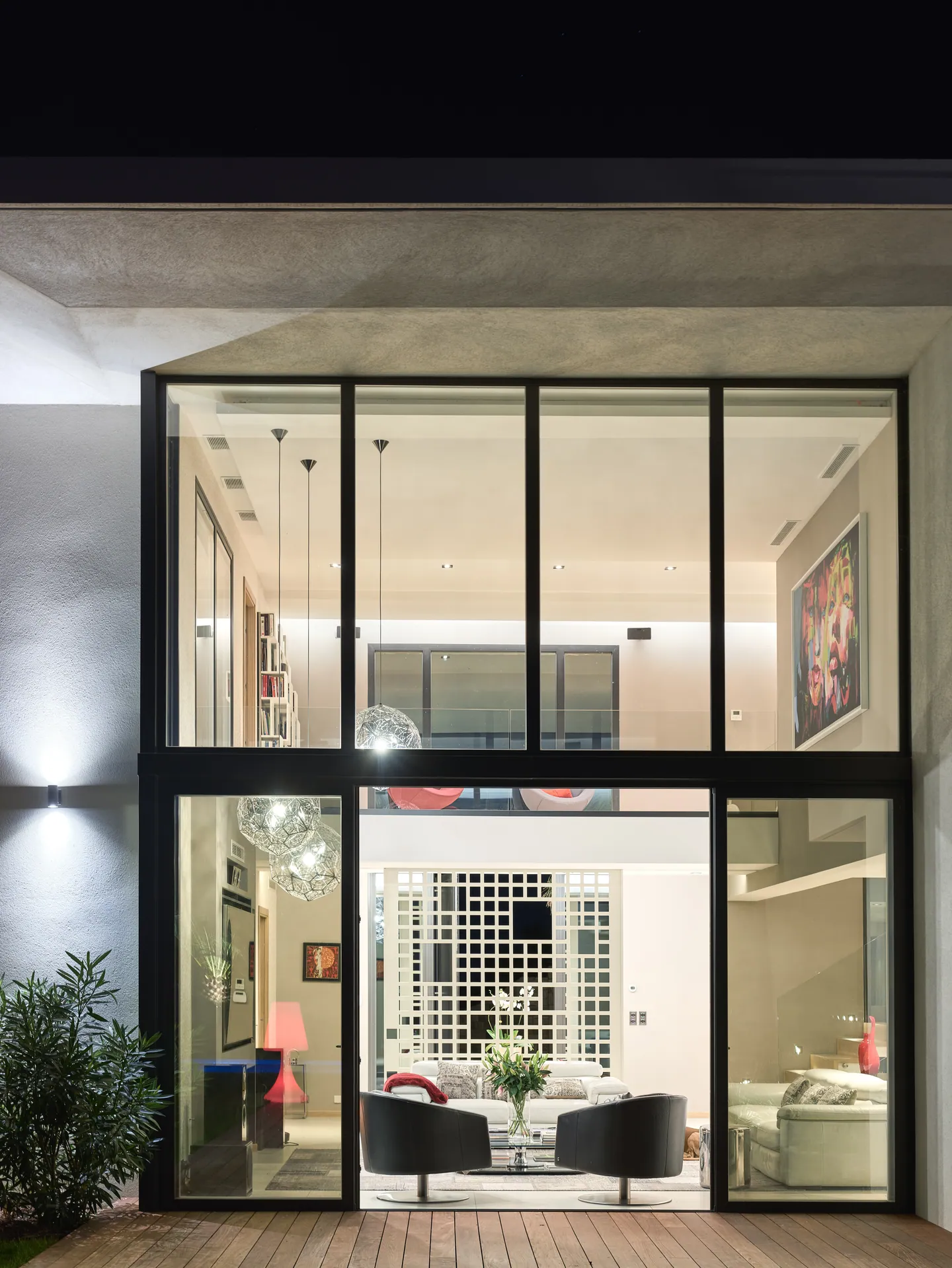 Double-height glazing at night revealing the lit lounge