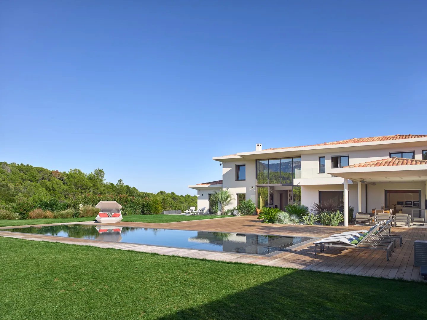 Lawn, pool and timber deck in front of the villa, wooded hills to the left