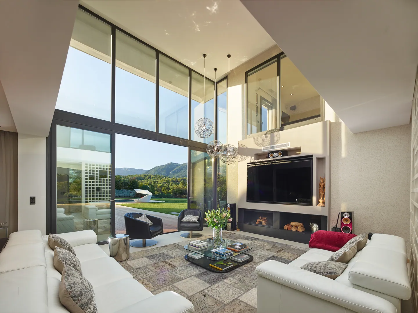 Double-height living room with white sofas, pendant lights and mountain view
