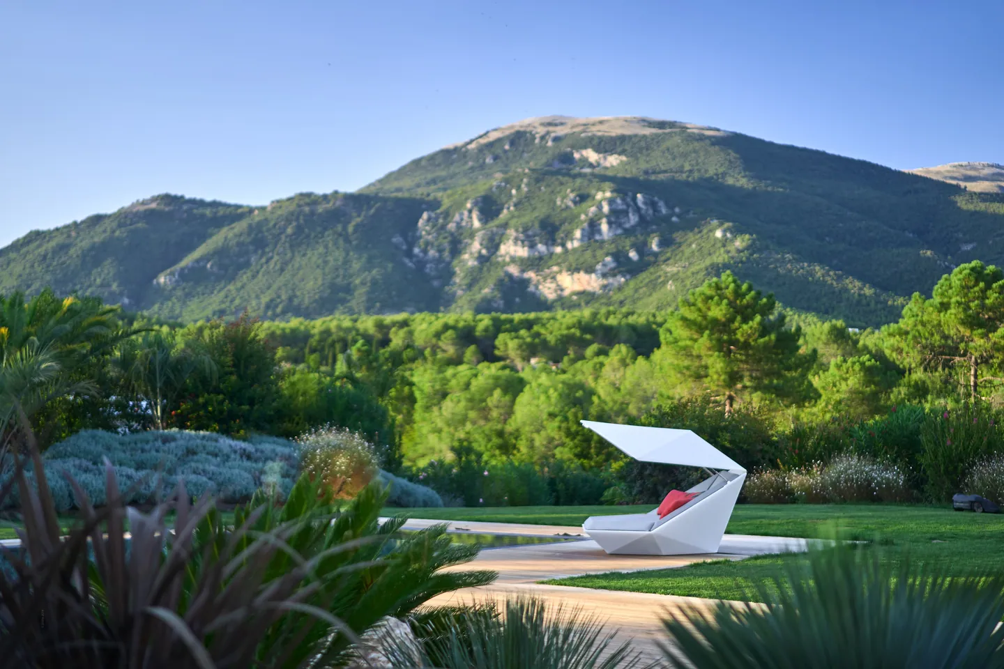 White designer daybed beside the pool, wooded mountain behind