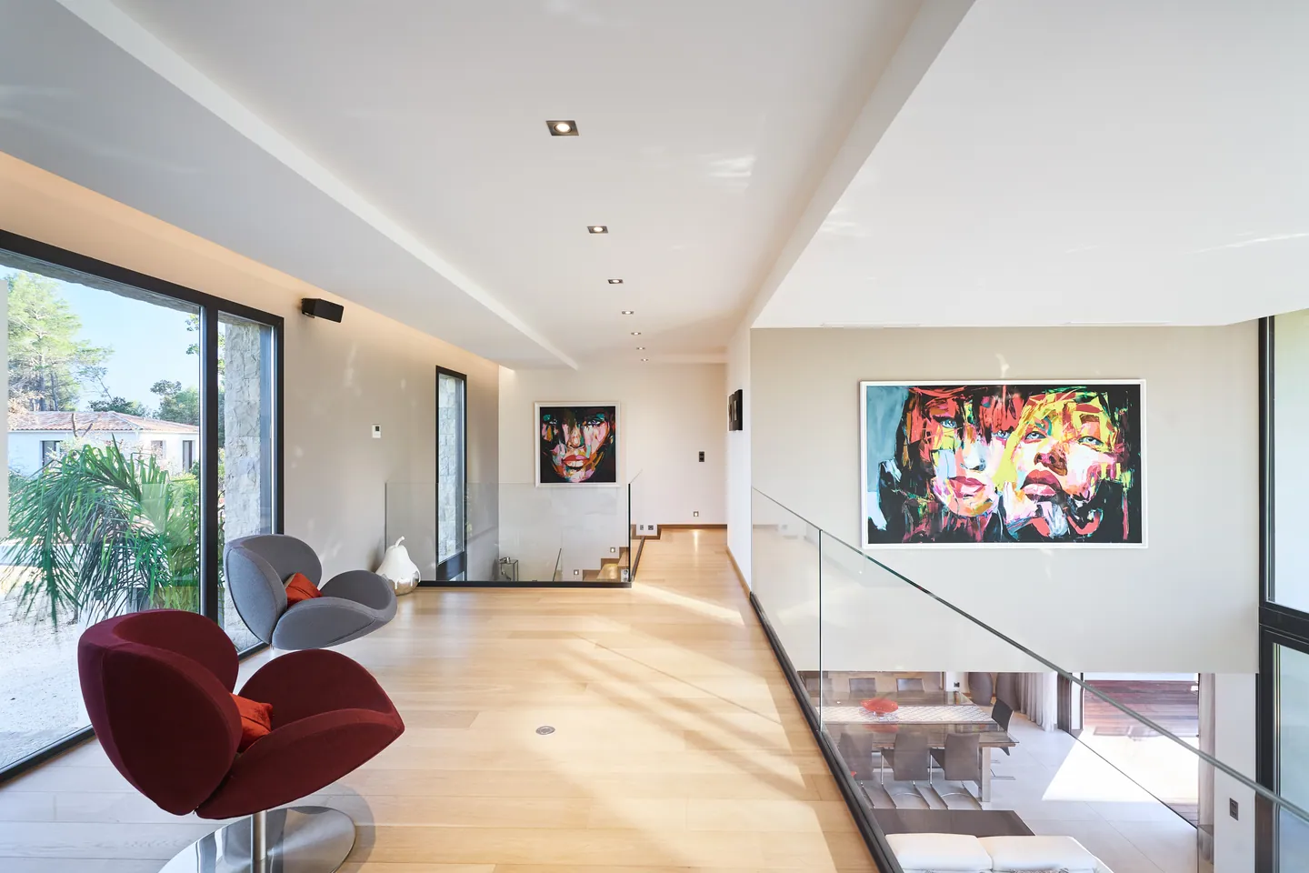 Mezzanine corridor with red armchairs, paintings and glass balustrade