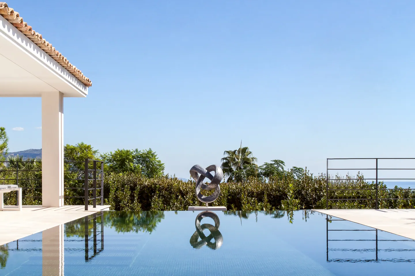 Metal sculpture at the edge of the infinity pool, greenery and sea in the distance