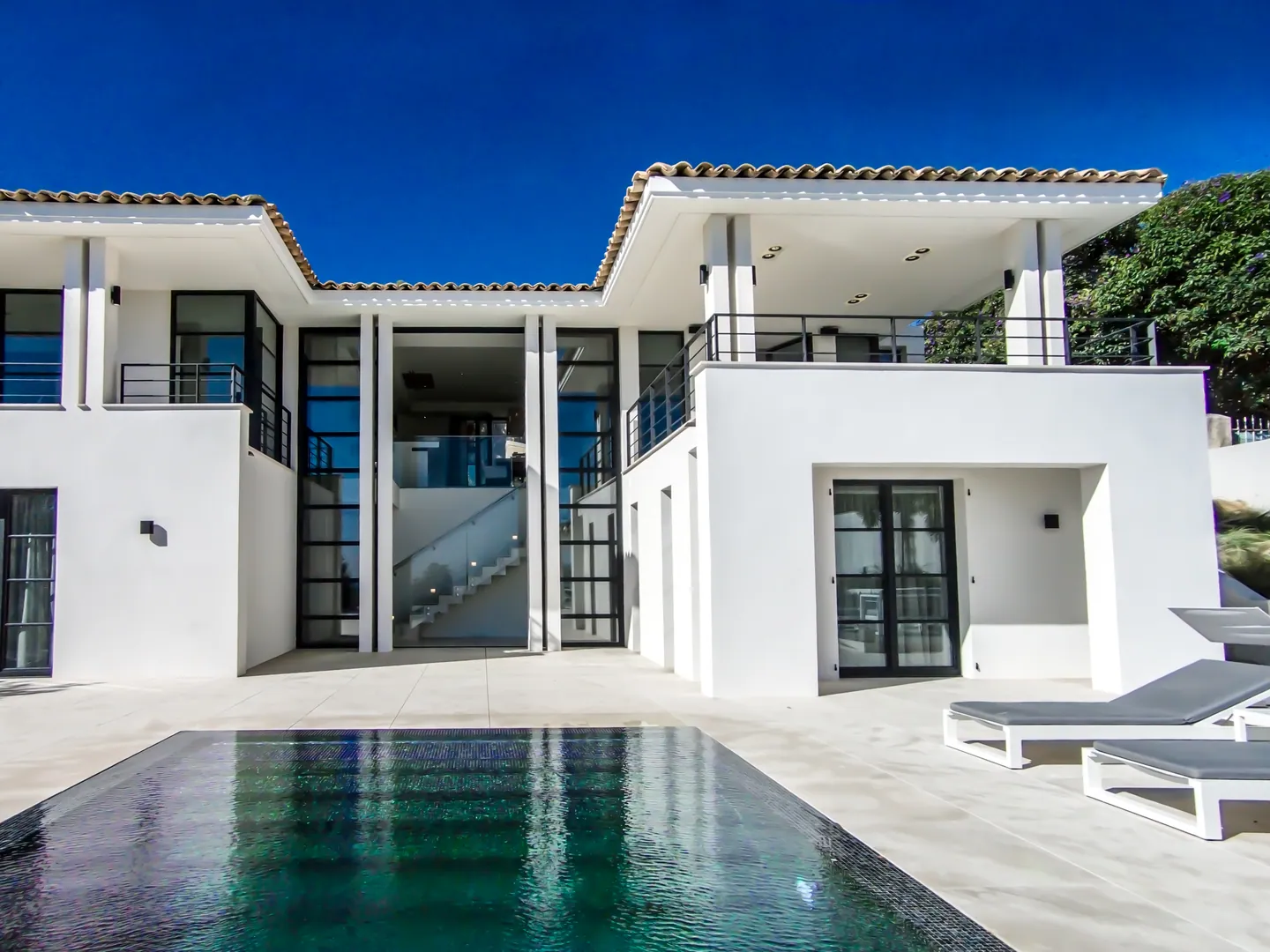 White facade with central glazing revealing the staircase, pool and loungers