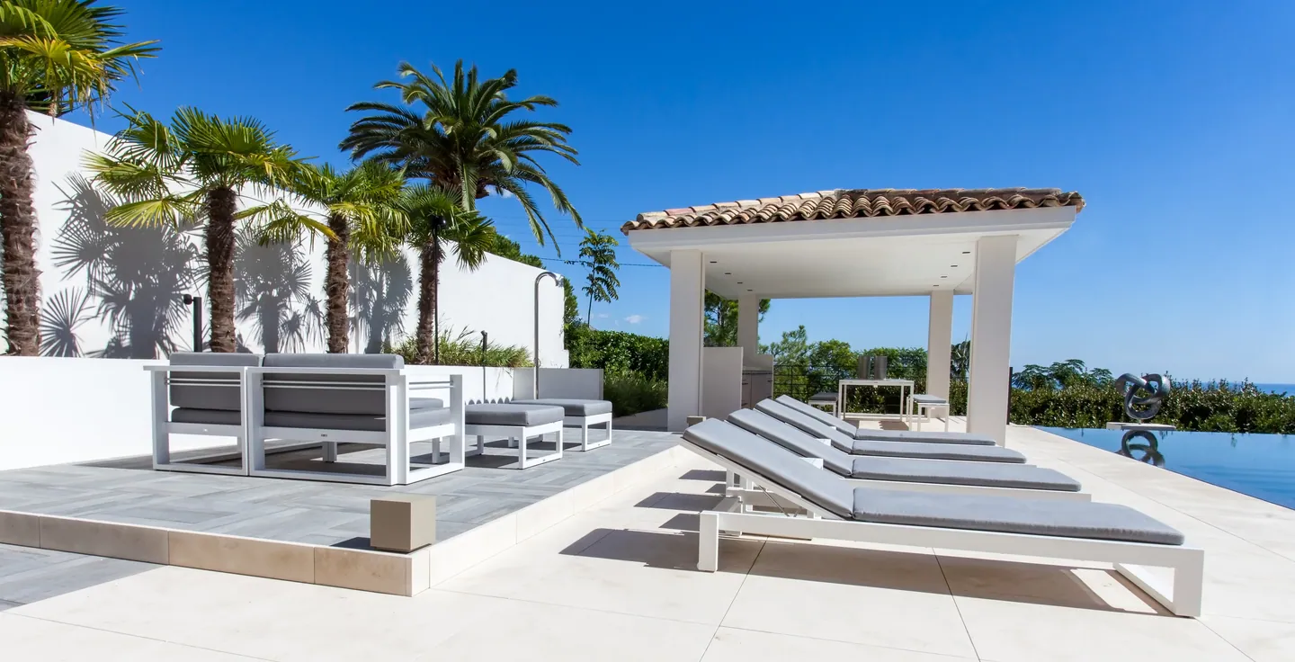 White outdoor lounge and loungers near the pool house, palm trees and infinity pool