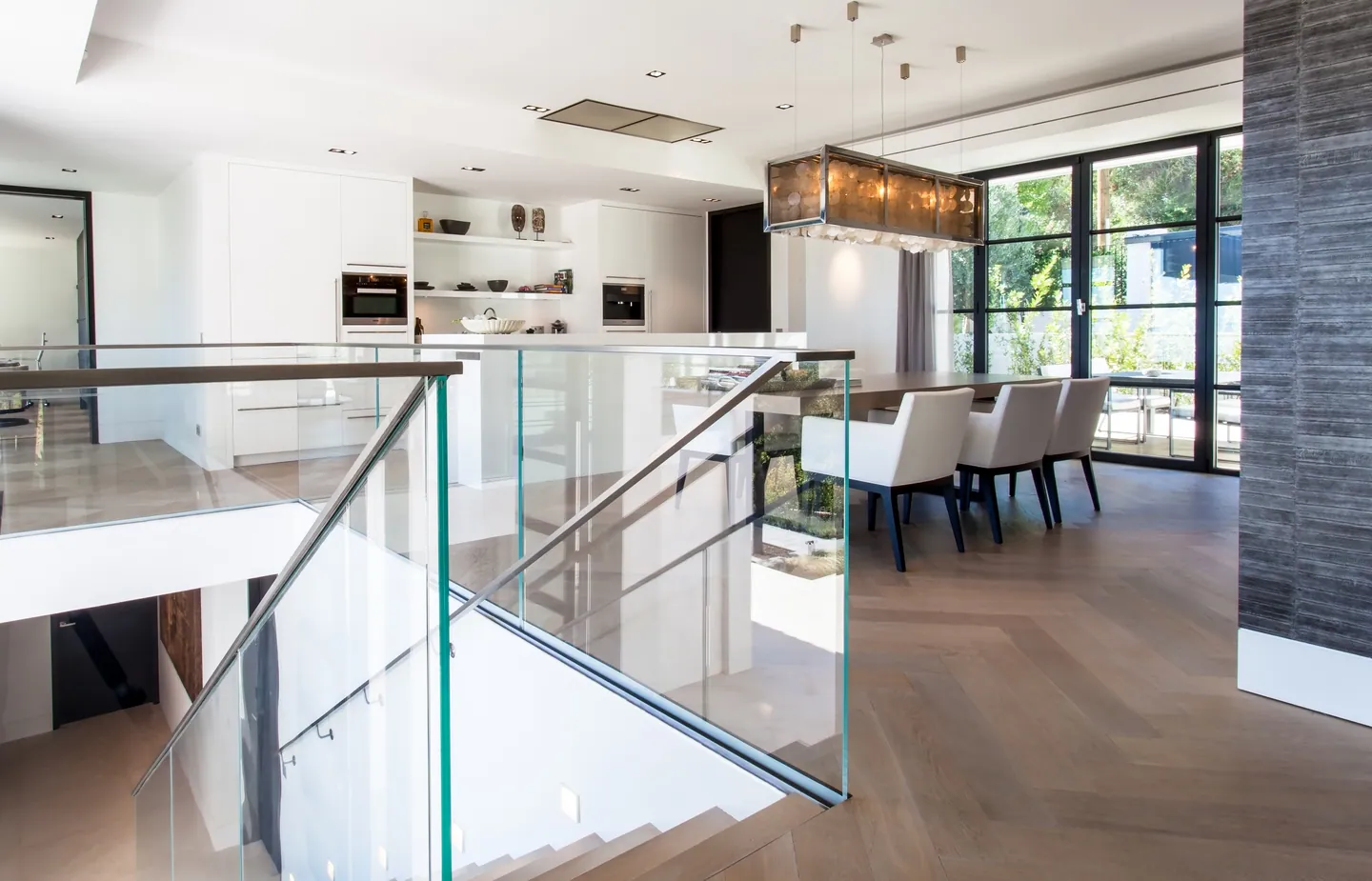 White kitchen and dining area seen from the glass-railed staircase, herringbone parquet