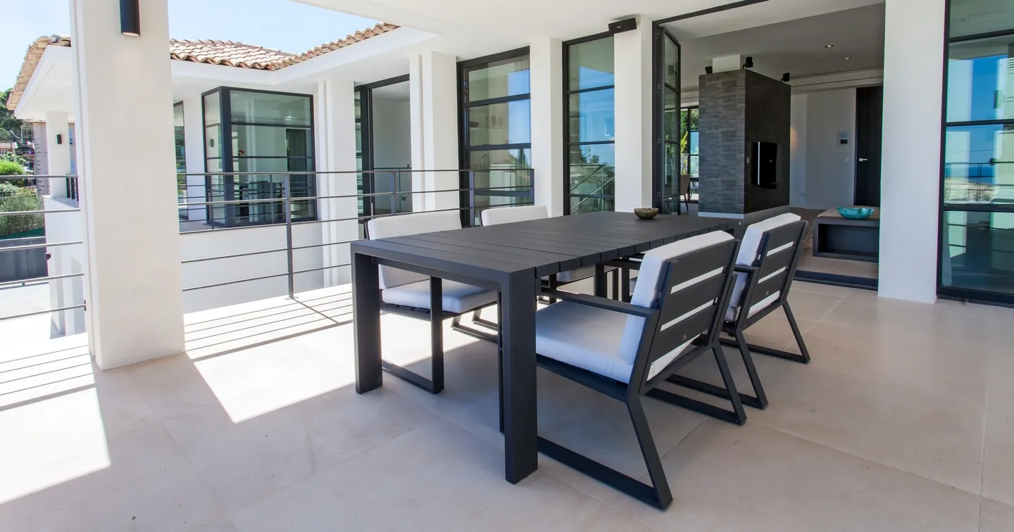 Covered terrace with outdoor dining table and chairs, windows open to the living room