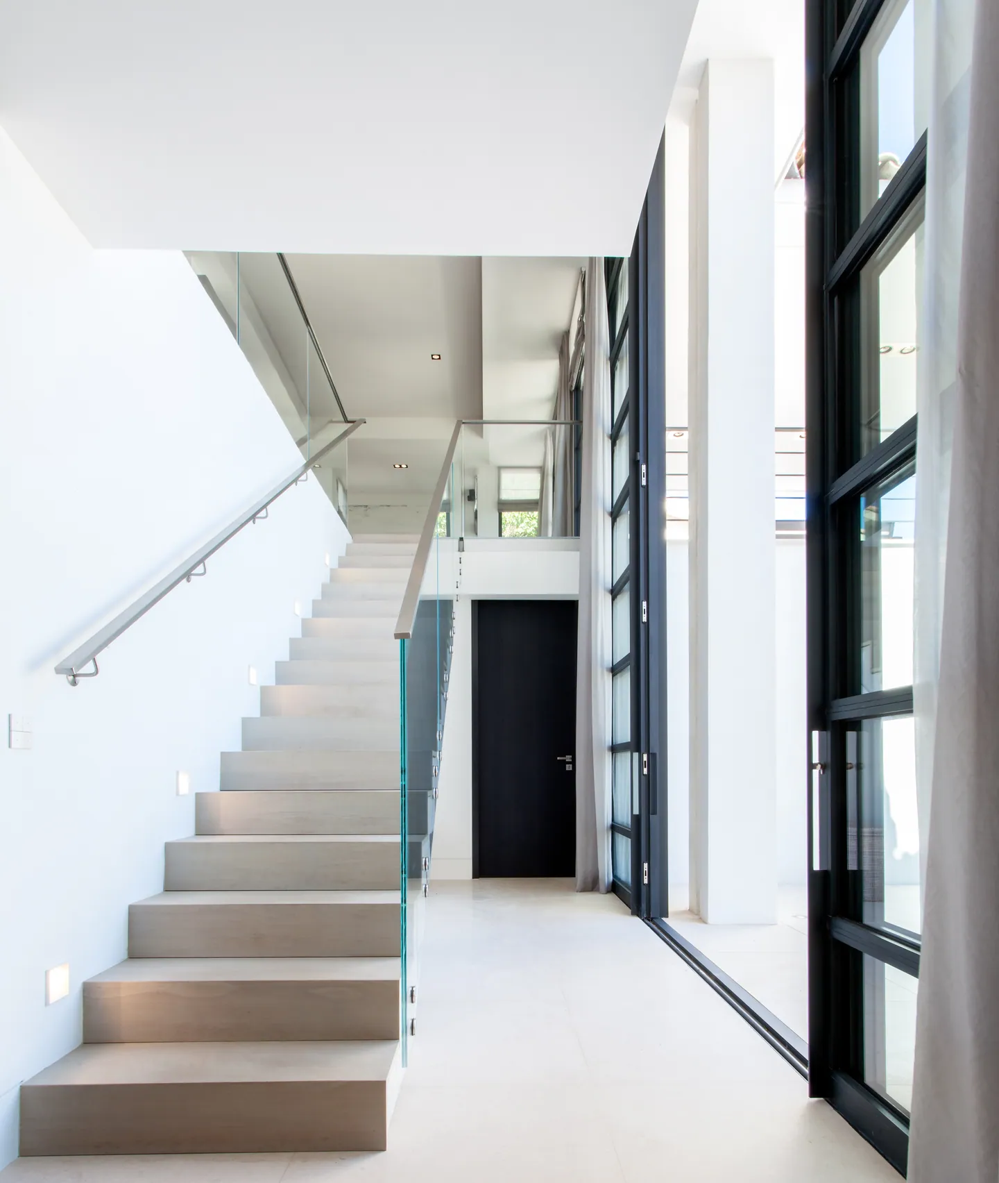Staircase with pale steps and glass balustrade alongside tall glazed panels