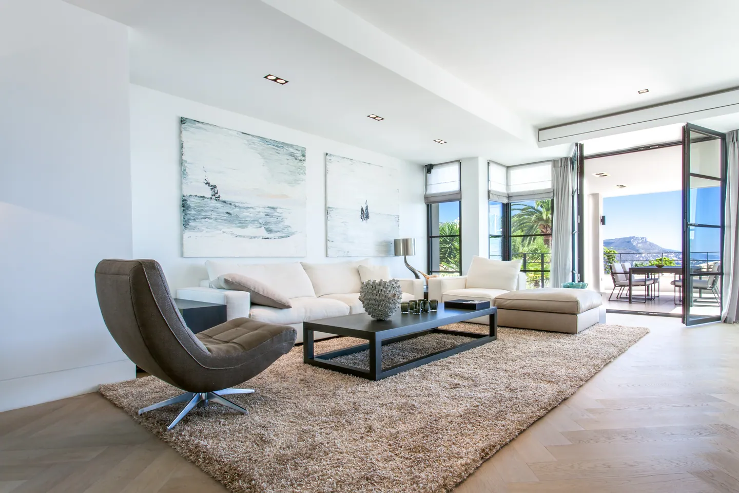 Bright living room with white sofa, large paintings and French doors onto the terrace