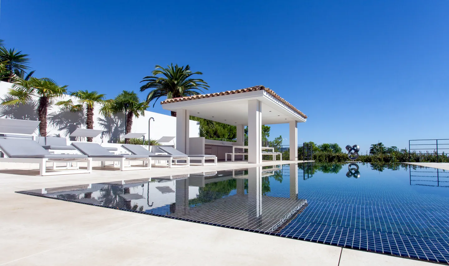 Blue mosaic infinity pool reflecting the pool house and palm trees