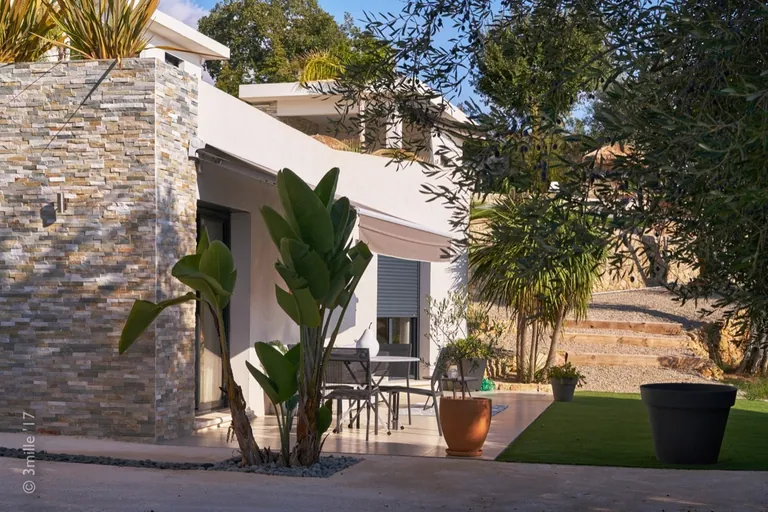 Side wing with stone cladding and a small terrace shaded by an awning