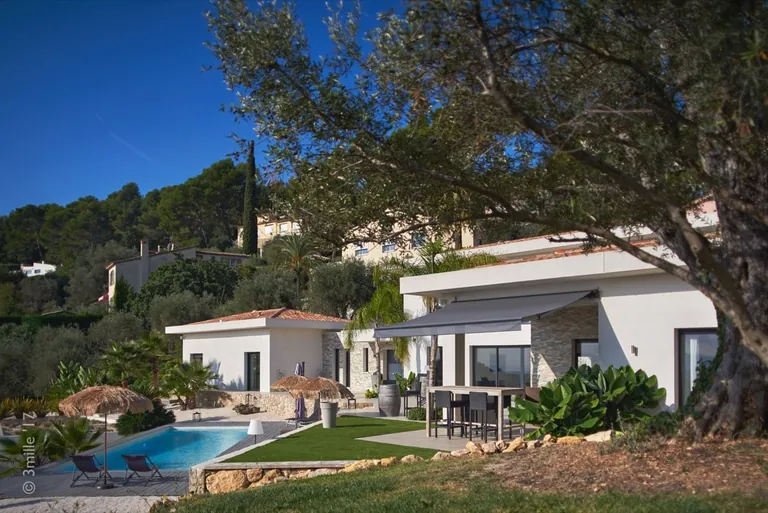 Villa seen from the garden beneath an olive tree, with pool and high table under an awning