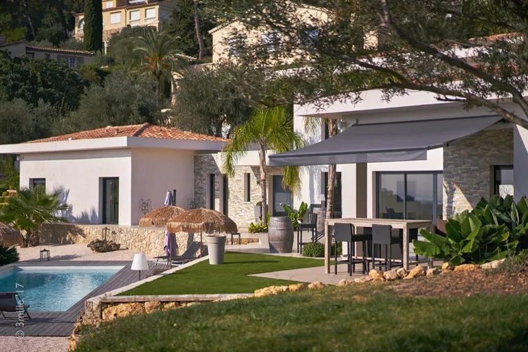 Lawn, pool and outdoor dining area under an awning at the foot of the villa