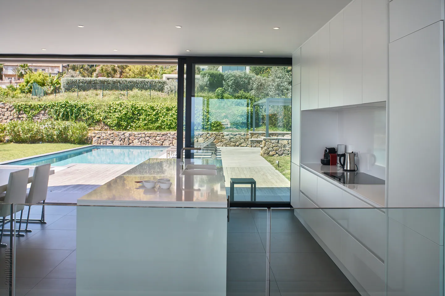 White kitchen island facing the glazing onto the pool and garden
