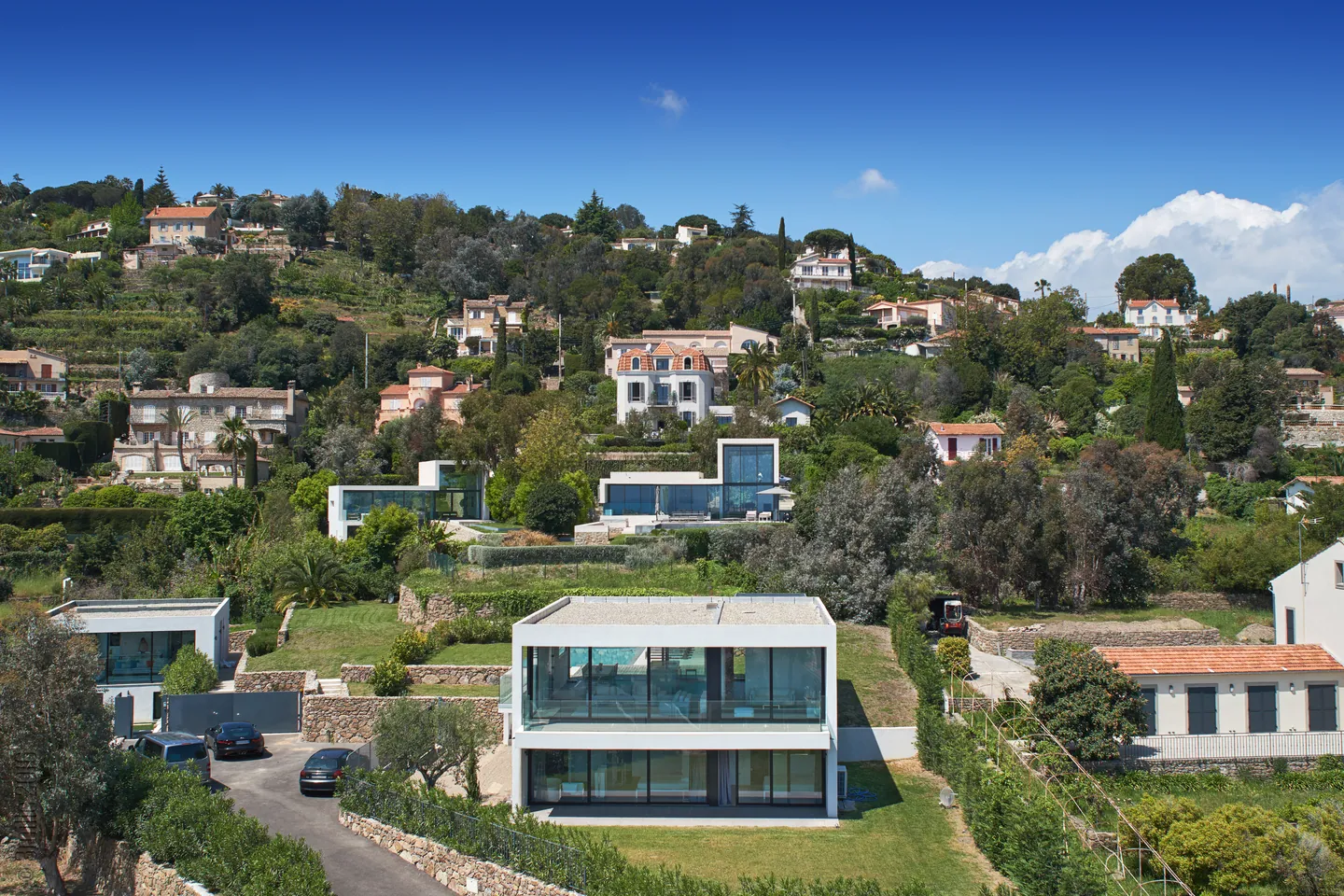 Façade vitrée sur deux niveaux de la villa cubique, nichée dans un coteau arboré