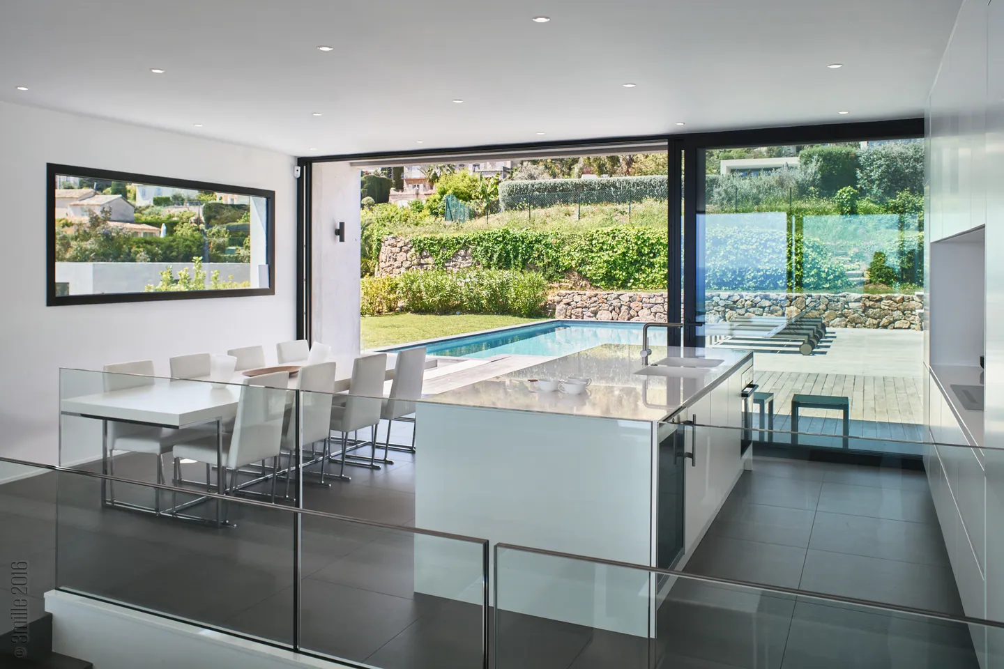 White island kitchen open to the pool, dining table and glass balustrade