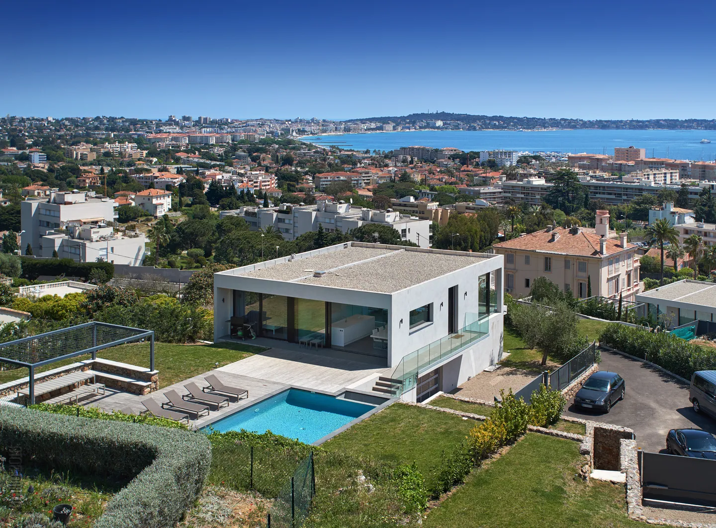 Elevated view of the white cubic villa with pool, garden and sea in the background
