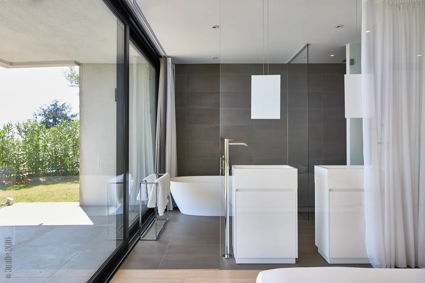 Open bathroom with freestanding bathtub, white basins and sheer curtains