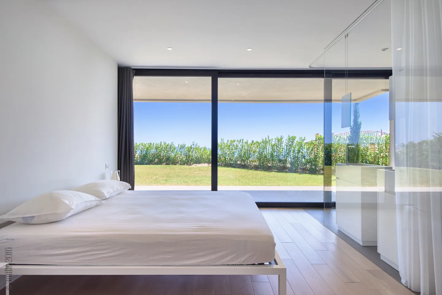 Minimalist bedroom with white bed and full-width glazing onto the lawn