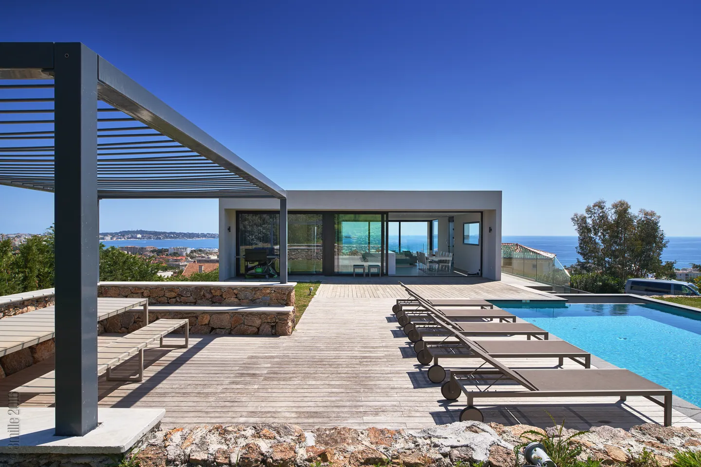 Louvred pergola and stone benches, wooden deck, pool and villa facing the sea